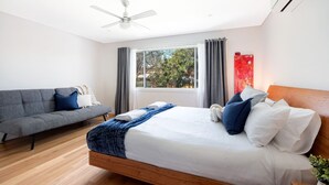 A modern bedroom with a bed, a grey sofa, a ceiling fan, and a window with curtains.