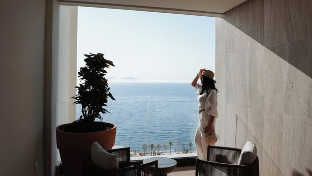 A balcony with a view of the sea, a potted plant, and a person standing by the railing. - Magnus Hotel (Vlorë)