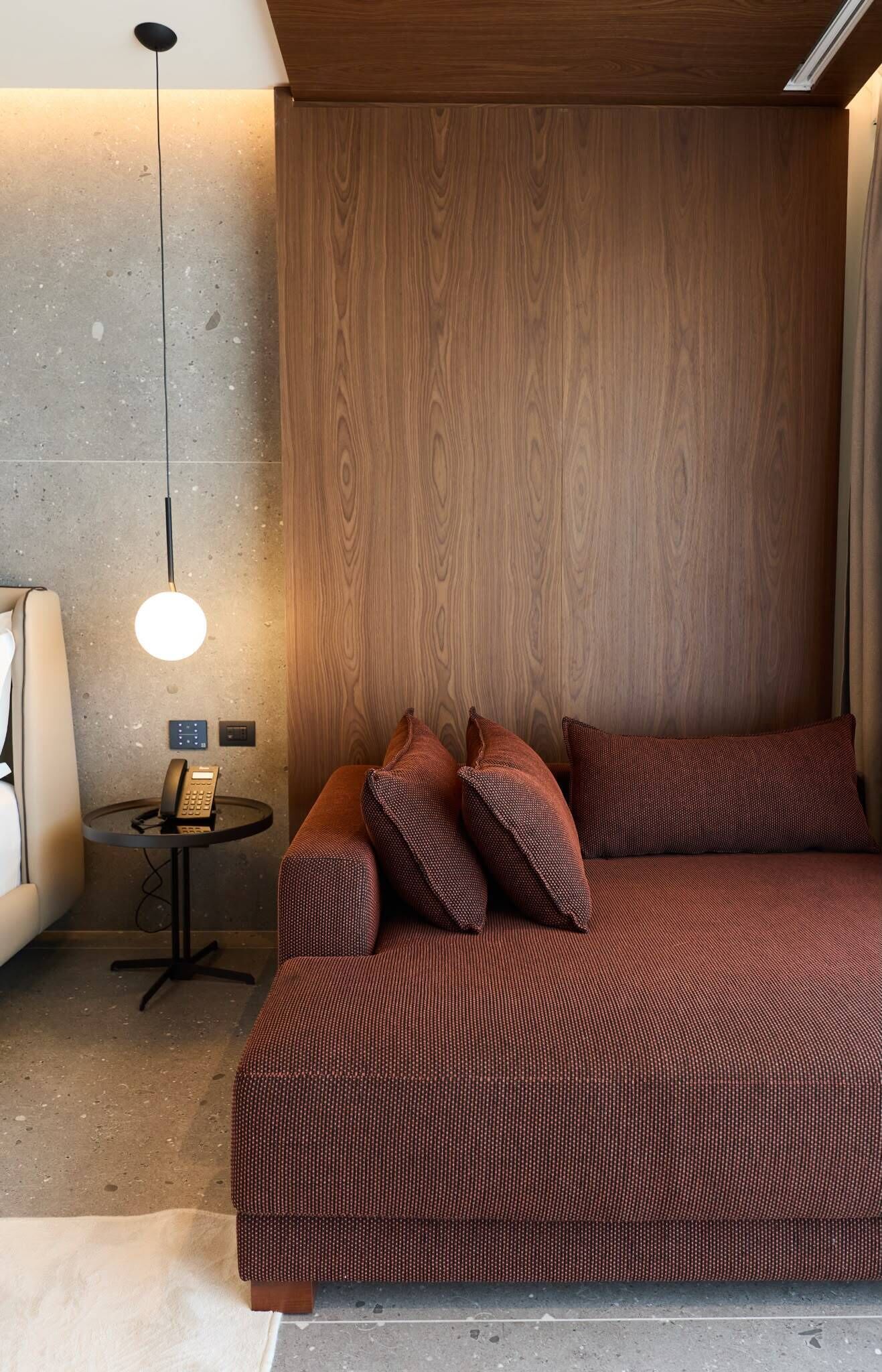 A modern bedroom with a wooden headboard, a round table with a telephone, and a patterned bedspread.