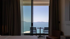 A hotel room with a bed, a small table, two chairs, and a view of the sea through a large sliding glass door. - Magnus Hotel (Vlorë)