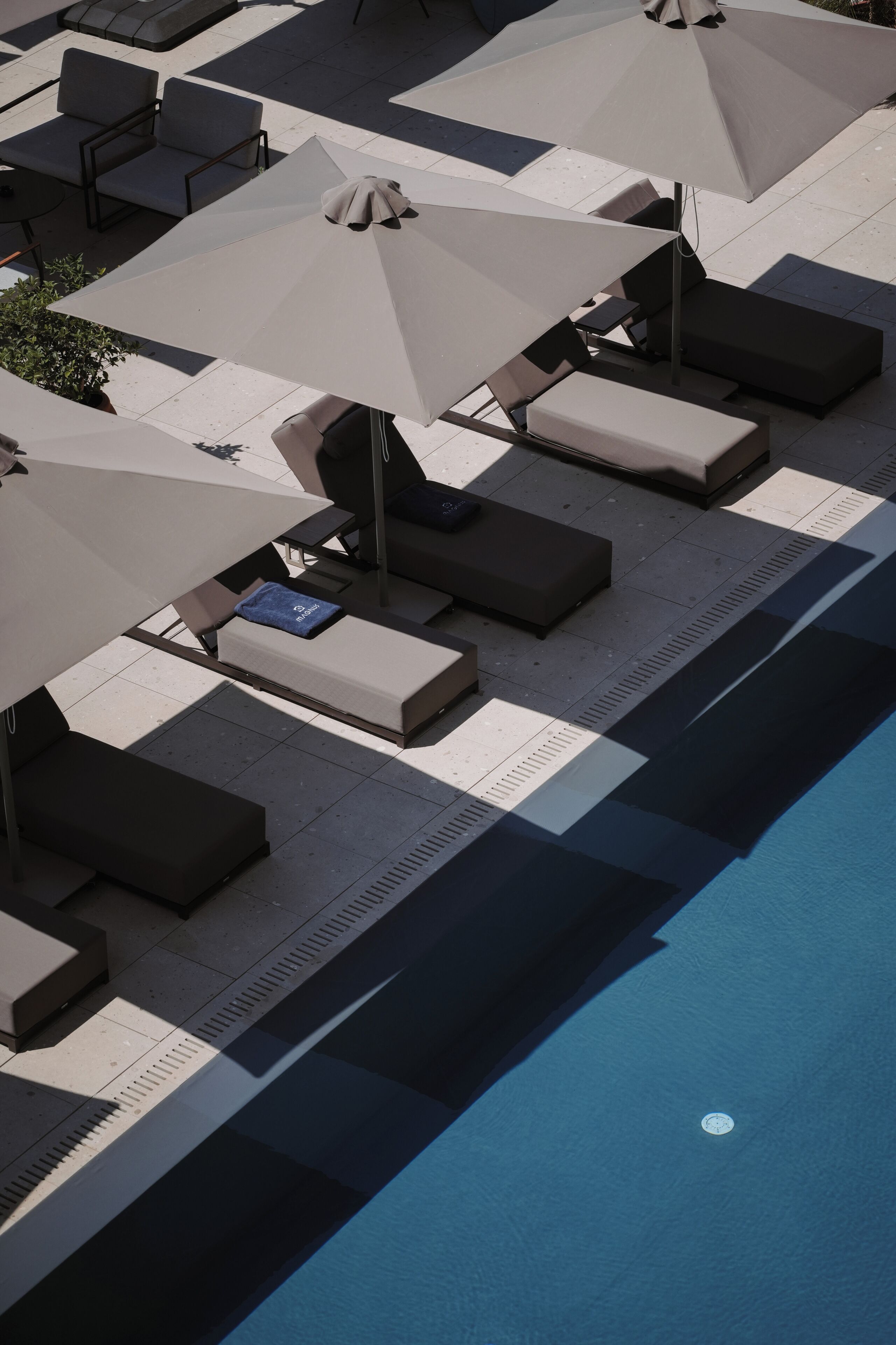 A poolside area with lounge chairs and umbrellas, a tiled floor, and a pool.
