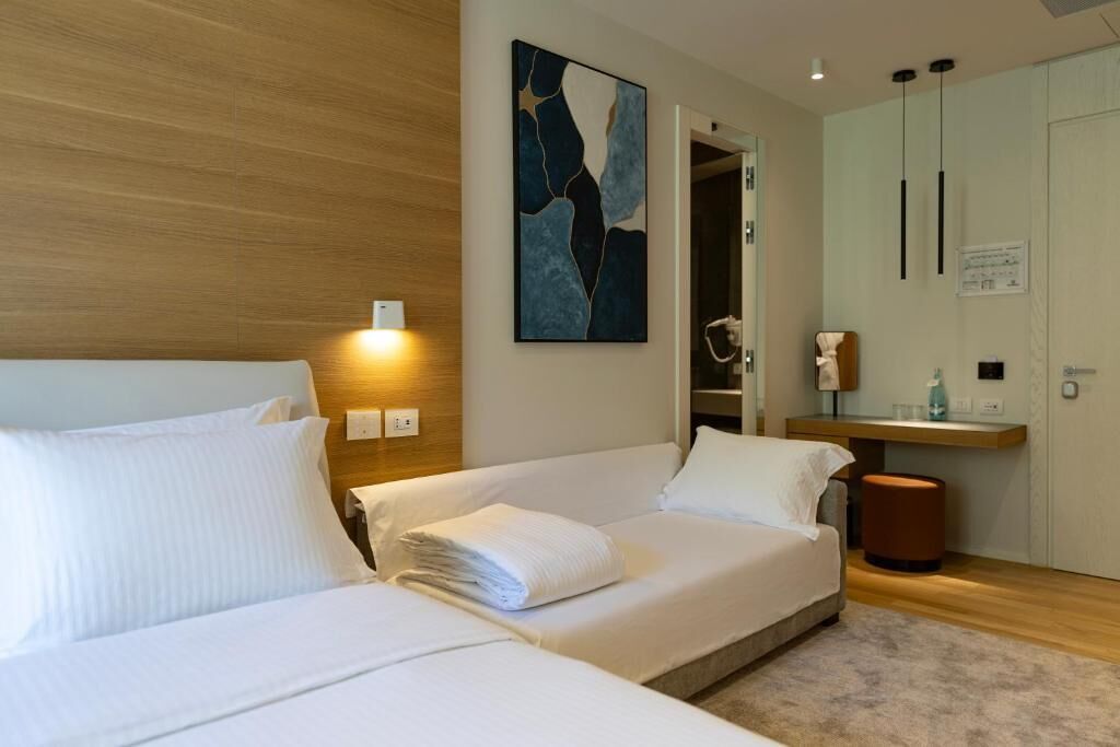 A hotel room with a bed, a bedside table, a mirror, and a wall-mounted artwork.