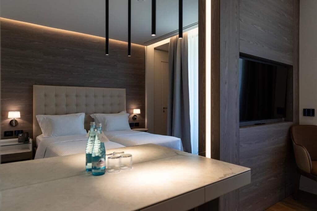 Una habitación de hotel moderna con una cama grande, mesitas de noche con lámparas, un escritorio con silla y una ventana.