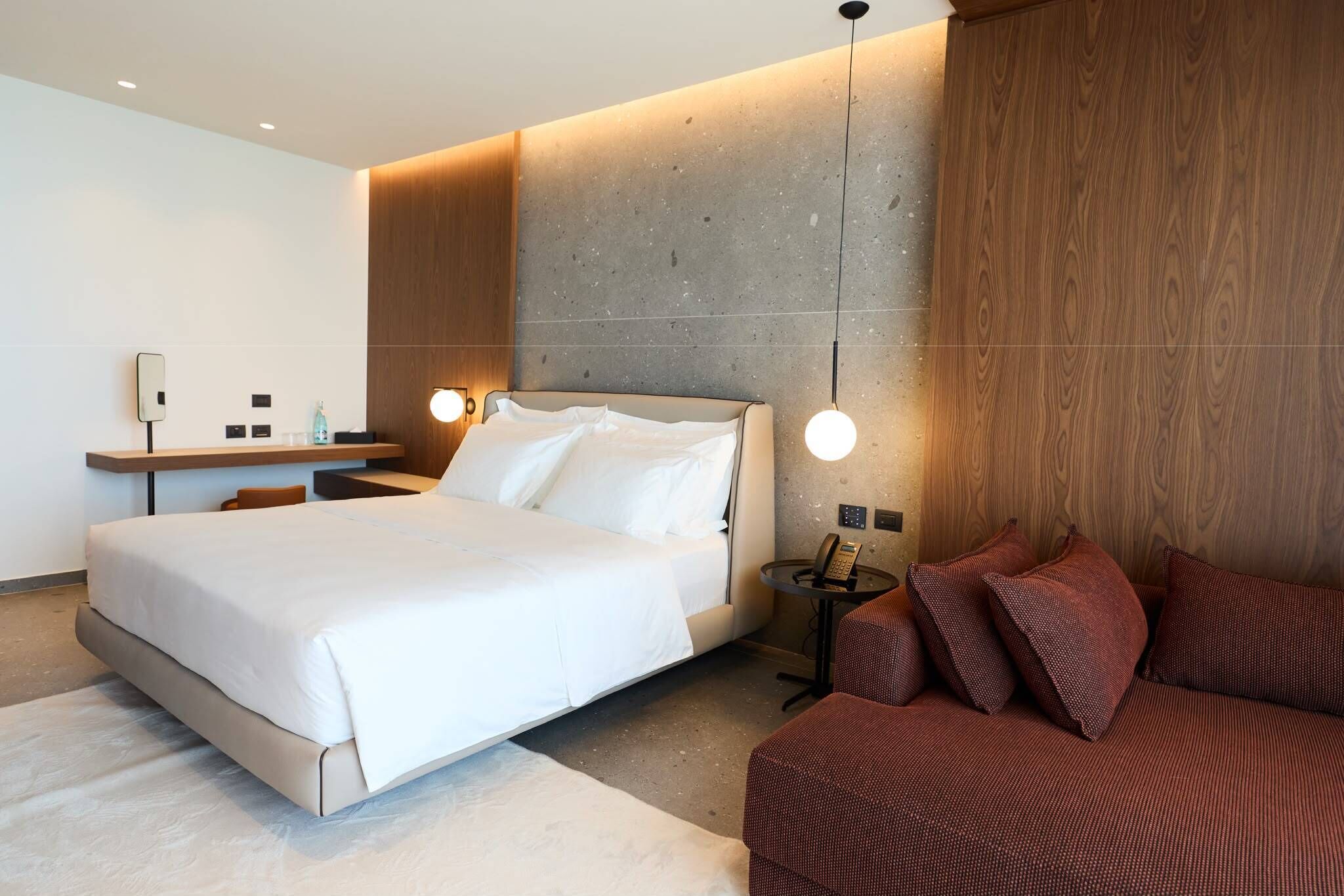 Ein modernes Hotelzimmer mit einem großen Bett, einem Schreibtisch, einer Couch und einem an der Wand befestigten Telefon.