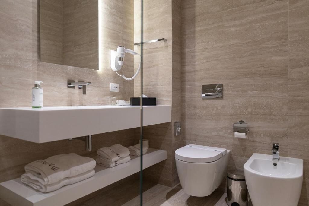 A modern bathroom with a glass shower enclosure, a white sink, a bidet, and a mirror above the sink.