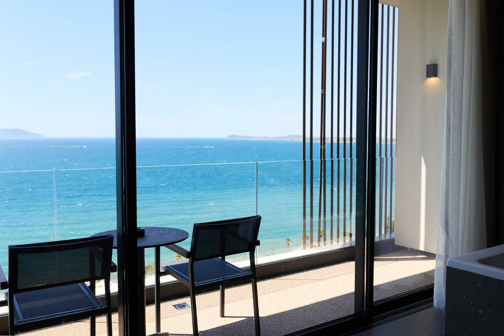 A balcony with a view of the sea, two chairs, and a table.