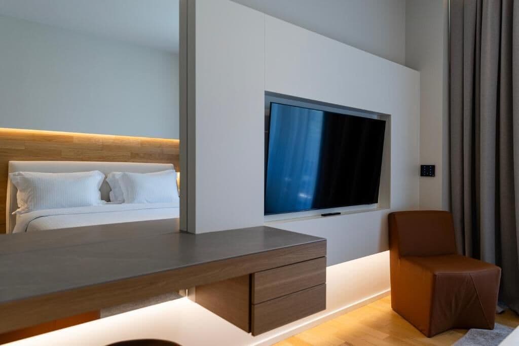 Et moderne hotelværelse med en seng, et fjernsyn monteret på væggen, et skrivebord med skuffer og en stol.