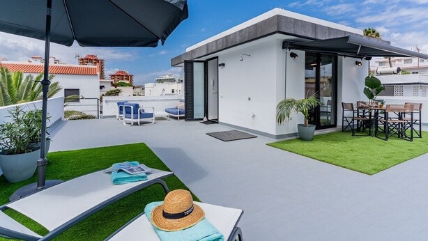 A rooftop terrace with a modern outdoor seating area, a small enclosed structure, and a view of the cityscape.