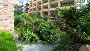 A hotel with multiple floors, outdoor balconies with plants, and a lush garden area with a water feature.