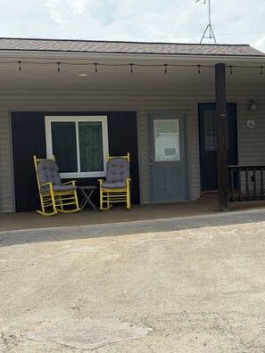 A building with a porch, two rocking chairs, a small table, and a door. - Welcome to Little Creek Ranch - A cozy cottage in charming Franklin (Franklin)