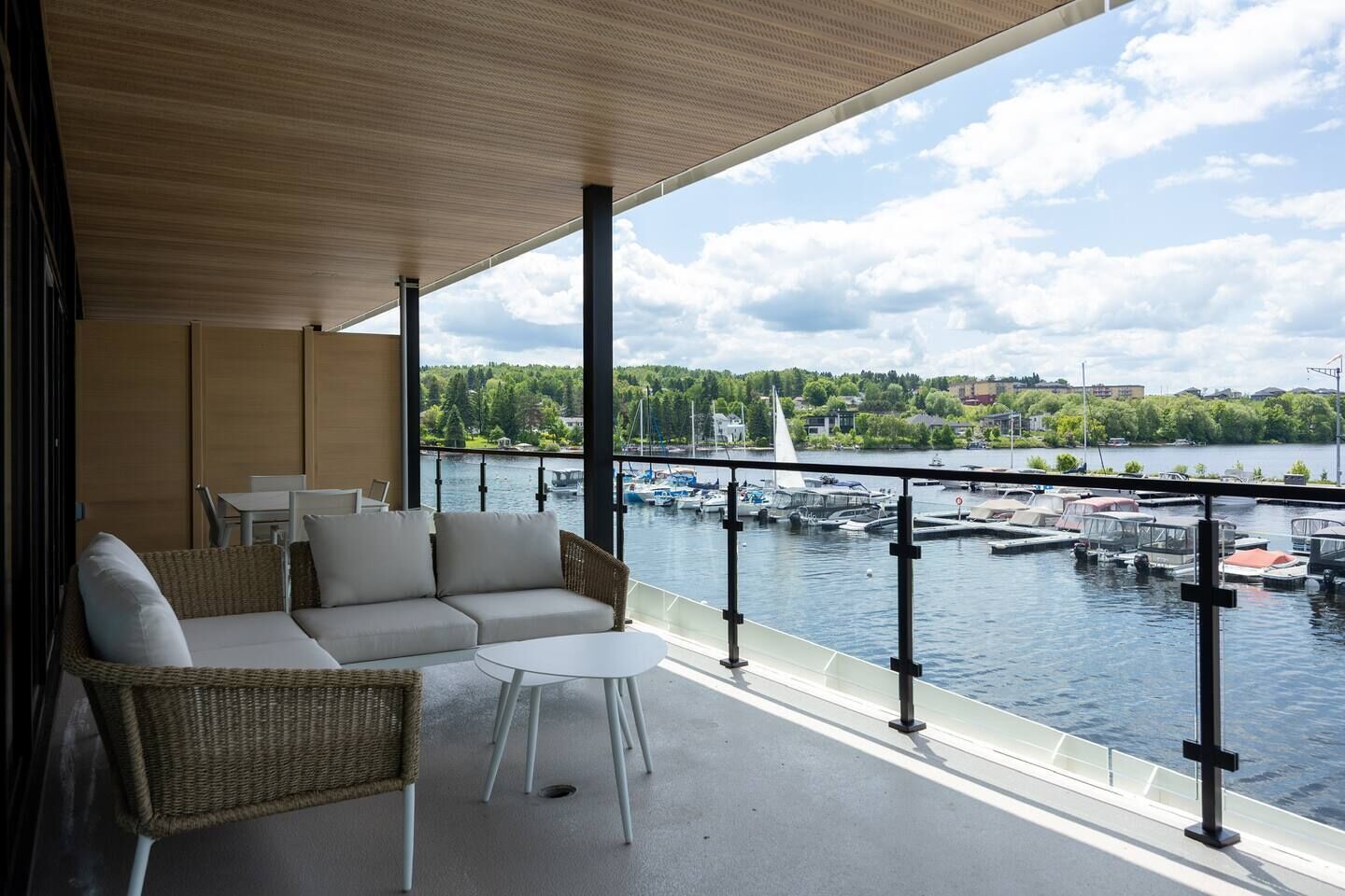 A balcony with a sofa and chairs, overlooking a marina with boats and a lake.