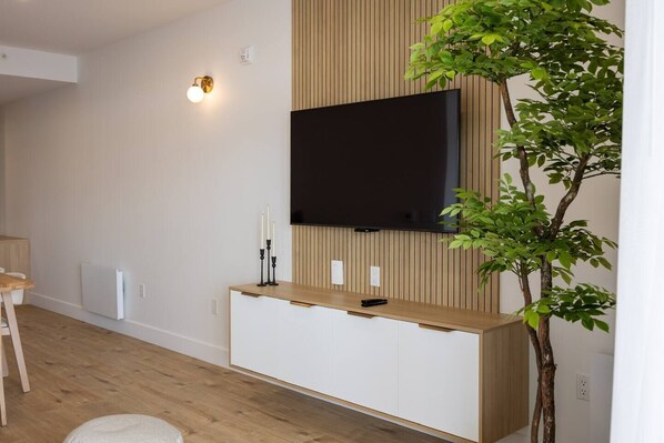 Ein modernes Wohnzimmer mit einem flachbildfernseher an einer Holzwand, einem weißen Schrank darunter und einer Zimmerpflanze zur Rechten.