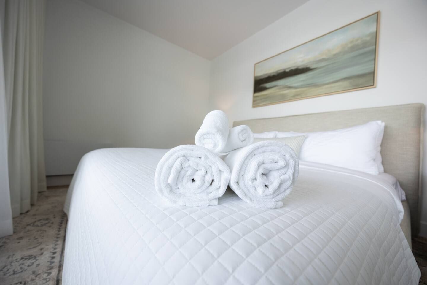 Ein Hotelzimmer mit einem großen Bett, weißer Bettwäsche und zwei aufgerollten Handt üchern auf dem Bett.