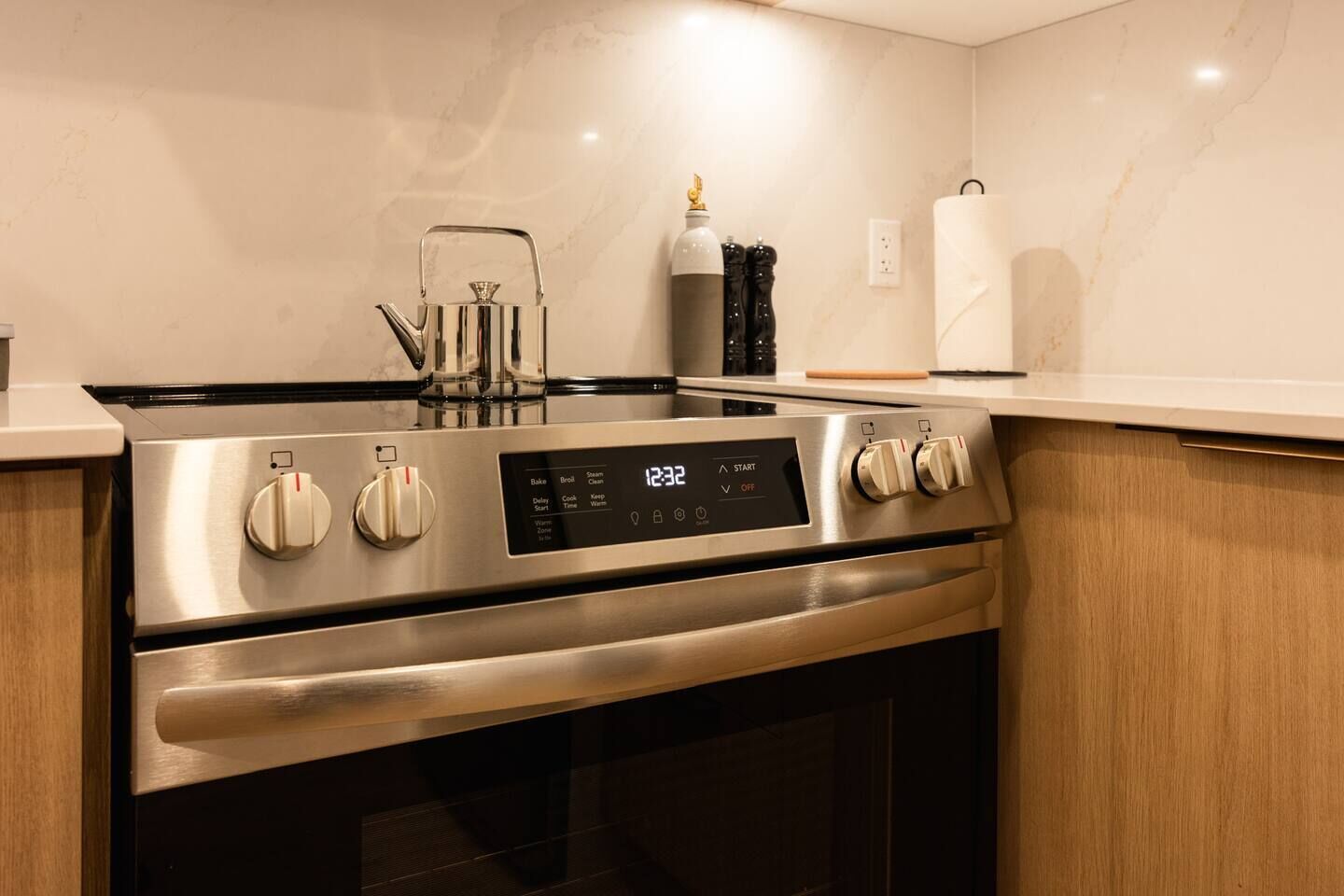 A stainless steel kitchen with a digital clock displaying 12:32, a kettle, and a coffee maker.