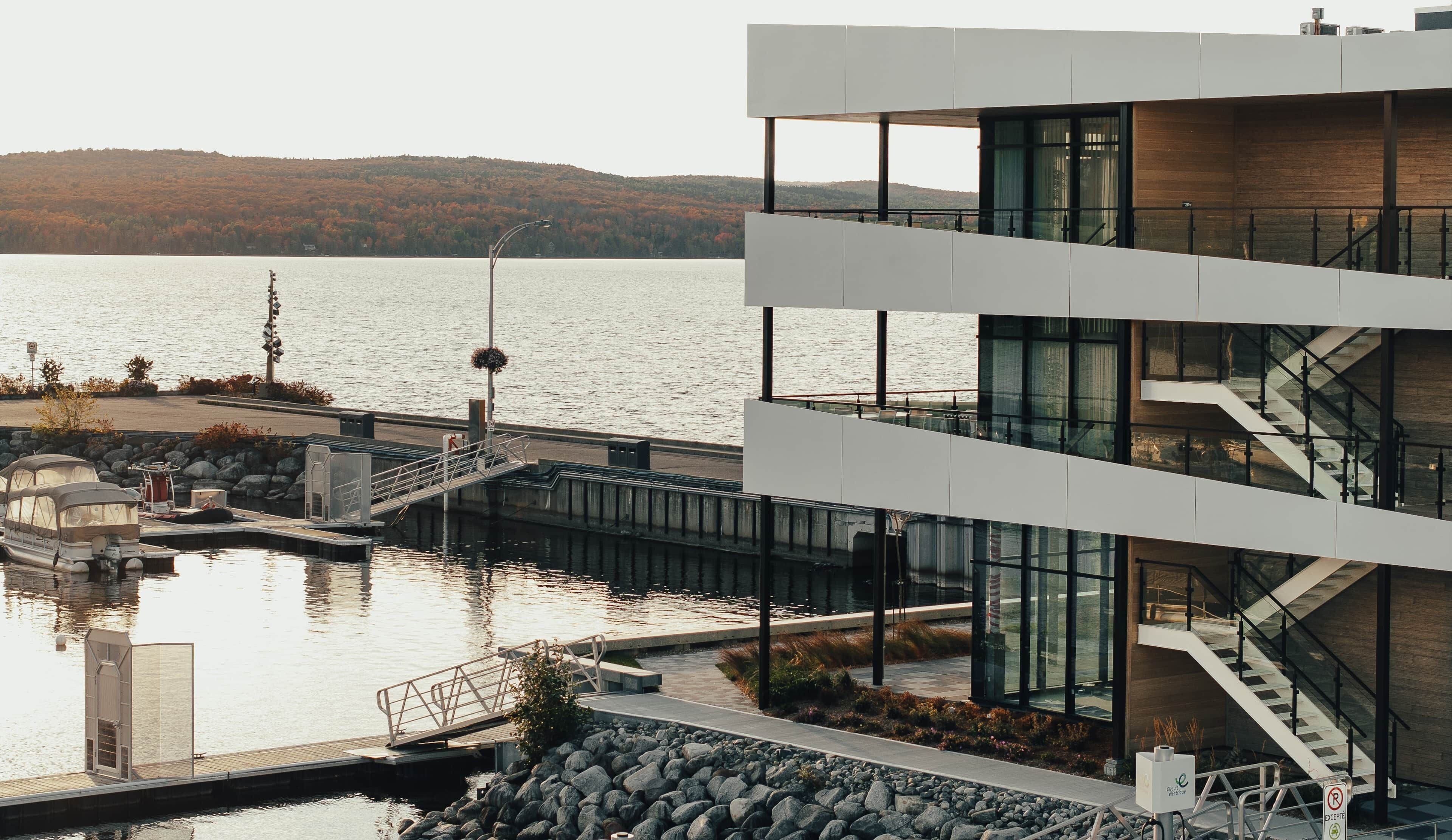 A modern building with a glass facade, a dock, and a view of a lake with hills in the background.