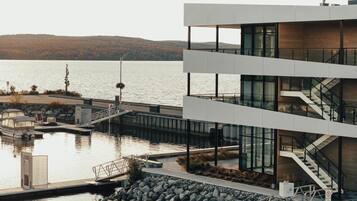 A modern building with a glass facade, a dock, and a view of a lake with hills in the background.