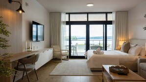 Una habitación de hotel moderna con una cama grande, un escritorio y un televisor. Tiene un balcón con vista al agua.