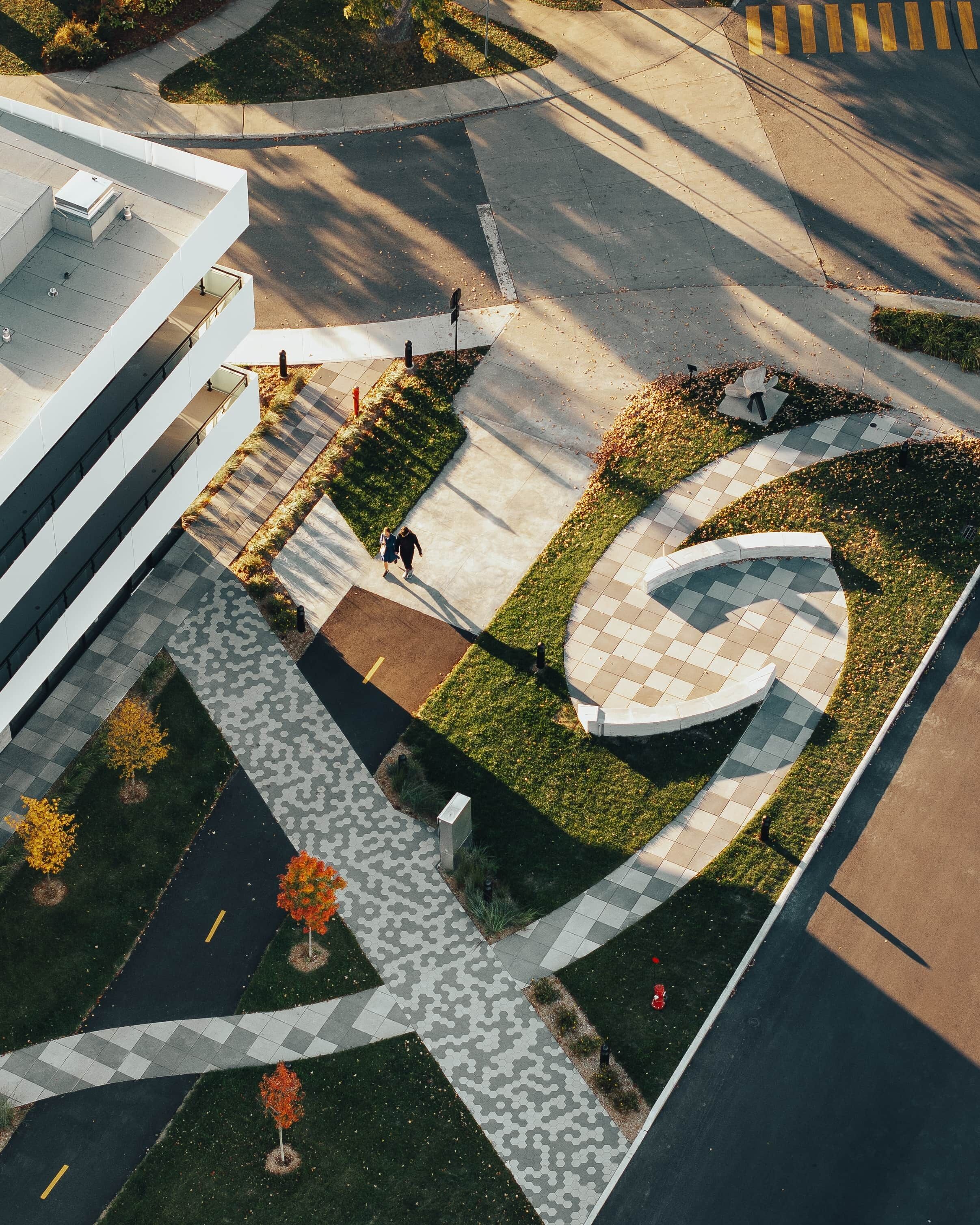 An aerial view of a landscaped area with a winding pathway, a circular garden feature, and a modern building with a flat roof.