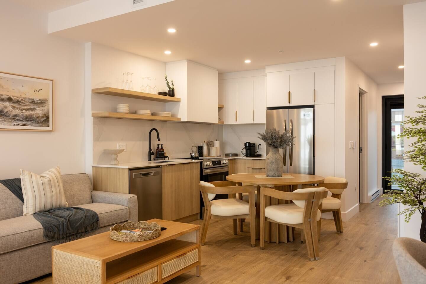 Une cuisine moderne avec des meubles blancs, un réfrigérateur en acier inoxydable et un coin repas comprenant des chaises et une table en bois.