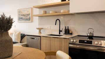 Een moderne keuken met een vaatwasser, fornuis en spoelbak. Er is een houten eettafel met stoelen en een vaas met planten.