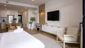 Una habitación de hotel moderna con una cama grande, un escritorio con una silla, un televisor montado en la pared y una kitchenette al fondo.