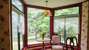 A room with large windows, a table with a vase of flowers, and two chairs.