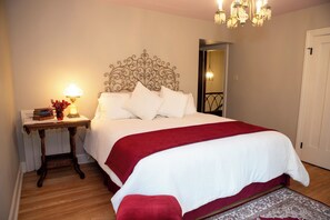 A neatly made bed with a white and red bedspread, a wooden nightstand with a lamp and books, and a chandelier above. - Marvelous lakefront 4-bedroom historical estate in Richfield with AC. (Richfield)