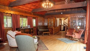 A cozy, wooden-furnished living room with a piano, two armchairs, and a bench.