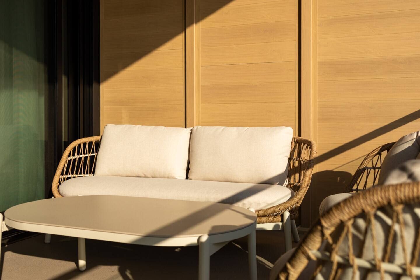 A wicker sofa with cushions, a small round table, and a wall with vertical blinds.