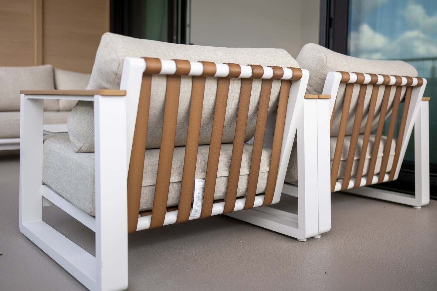 Deux chaises blanches, dotées d’un dossier à rayures marron et blanches et de coussins beige, sont posées sur un sol gris.