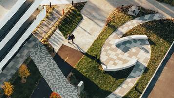 Luchtbeeld van een aangelegde omgeving met een slingerpad, een rond tuinornament en een modern gebouw met een plat dak.