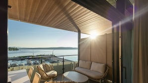Un balcone con sedie in vimini e un divano, con vista su uno specchio d'acqua e un pontile con barche.