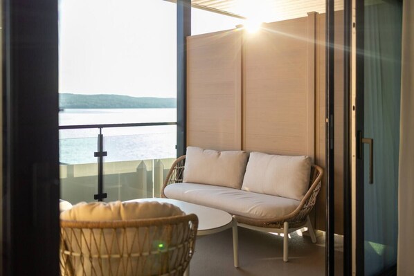 Un balcon avec un fauteuil en osier et un canapé donnant sur une étendue d’eau.