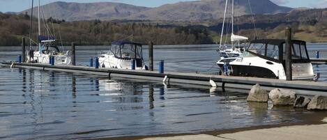 A marina with boats docked, calm water, and mountains in the background.