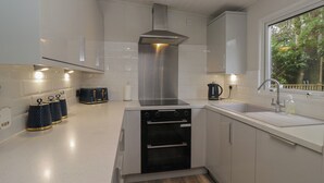 A modern kitchen with white cabinets, a stainless steel range hood, a built-in oven, and a window with a view of trees. - Jackos Lodge (Windermere)