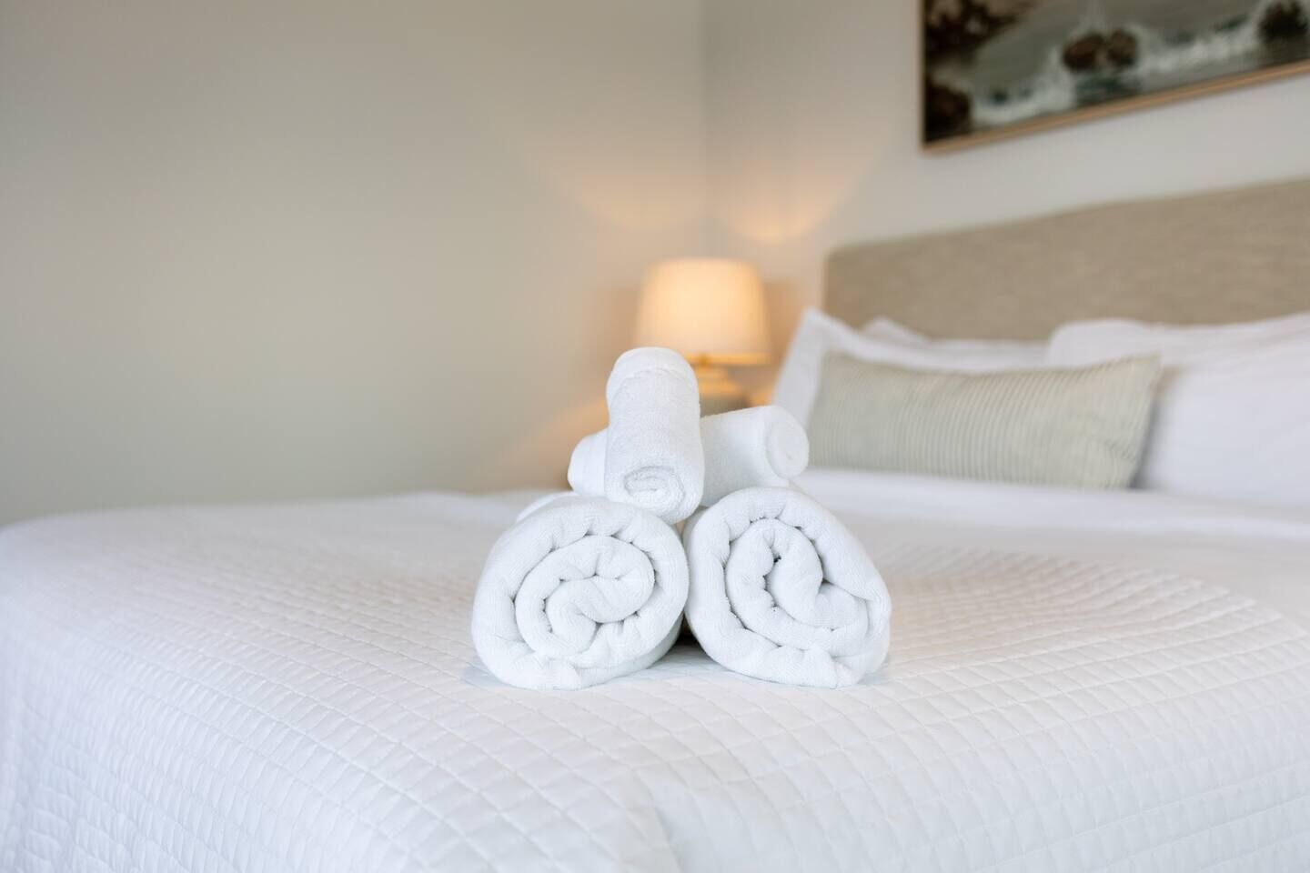 Un lit bien fait, avec des draps blancs et deux serviettes enroulées posées sur le dessus.