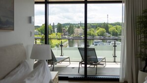 A room with a large window overlooking a river, a bed, a chair, and a table. - La Capitainerie - Marina - 304 - Bord de l'eau (Lac-Mégantic)