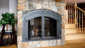 A stone fireplace with a glass door, a wooden staircase, and a potted plant. - Aux mille et une étoiles (Piopolis)