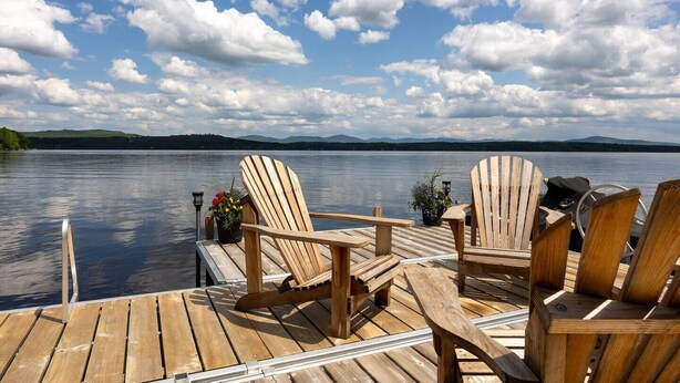 A wooden dock with two Adirondack chairs and a small table, overlooking a calm lake with mountains in the distance. - Aux mille et une étoiles (Piopolis)