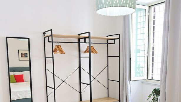 A bedroom with a bed, a wardrobe, a mirror, and a window with curtains.