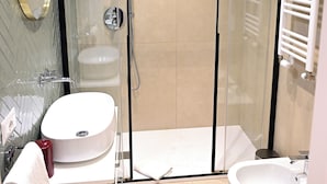 A modern bathroom with a glass-enclosed shower, a sink, and a bidet.