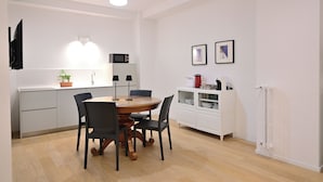 A modern kitchen with a dining table, chairs, a microwave, and a white cabinet with dishes.