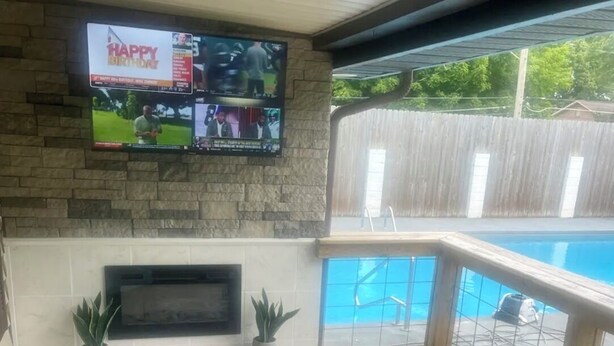 A covered patio with a TV mounted on the wall, a pool, and outdoor seating.