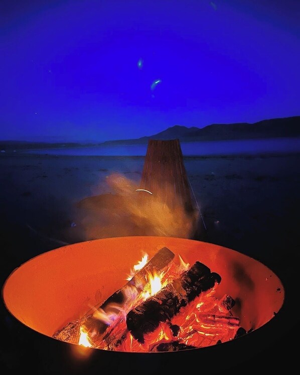 A campfire in a circular fire pit with a mountainous landscape in the background under a night sky.