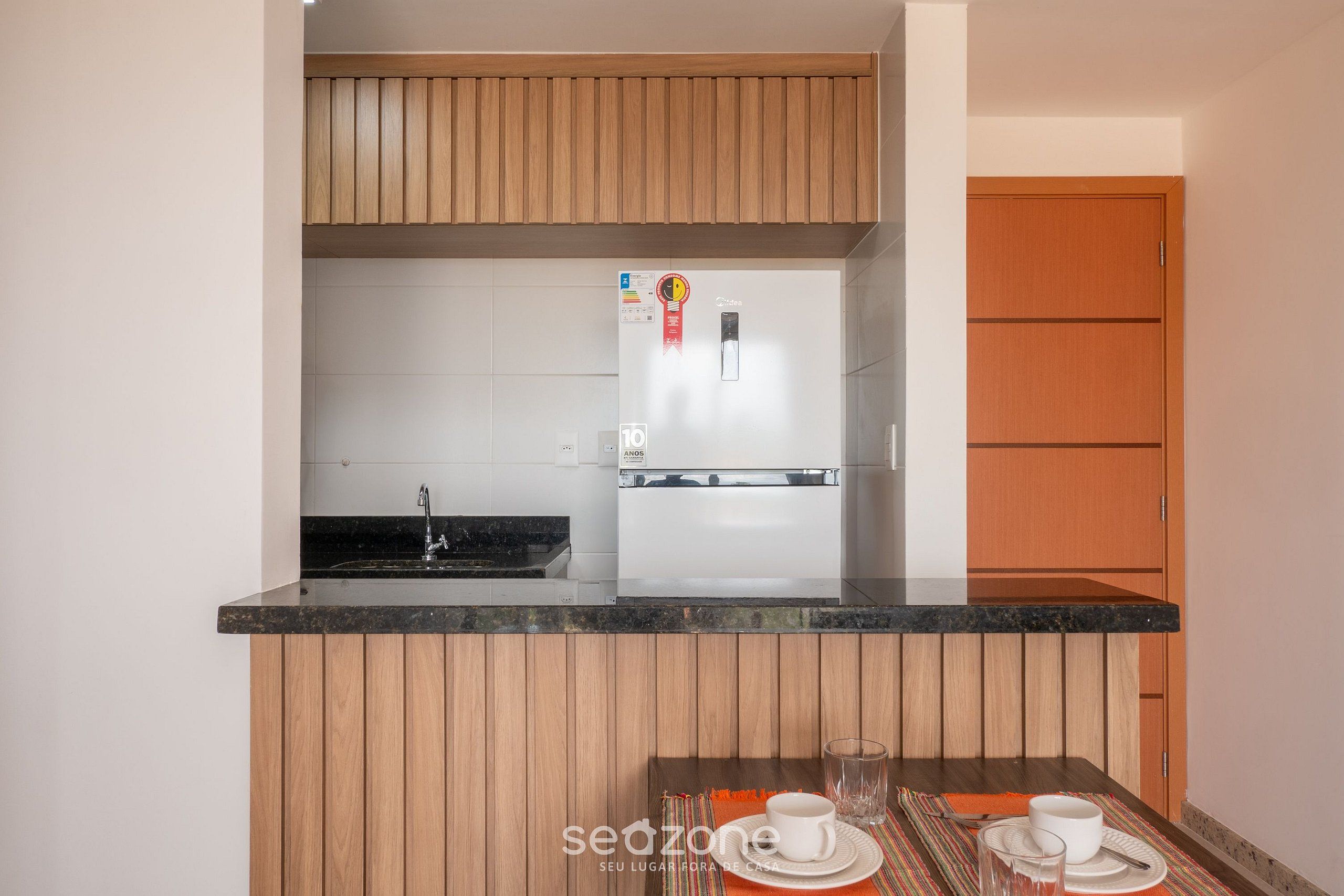 Una cocina compacta con armarios de madera, un refrigerador empotrado y un pequeño comedor con una mesa y sillas.