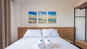 Een hotelkamer met een bed, twee kussens, een houten hoofdbord en drie wanddecoraties met een strandscène.