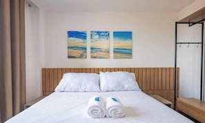 Une chambre d’hôtel avec un lit, deux oreillers et trois tableaux représentant une scène de plage, accrochés au mur.