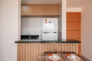 Une cuisine compacte avec des meubles en bois, un réfrigérateur encastré et un coin repas avec une table dressée pour deux personnes.