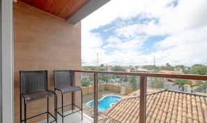A balcony with two wicker chairs, a swimming pool, and a view of the neighborhood.