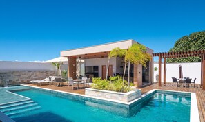 A poolside area with a covered seating area, a pool, and a pergola with plants.